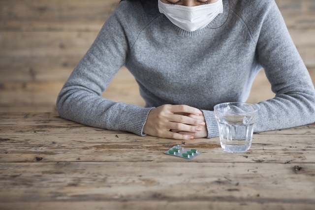 マスク姿で薬を飲もうとする女性